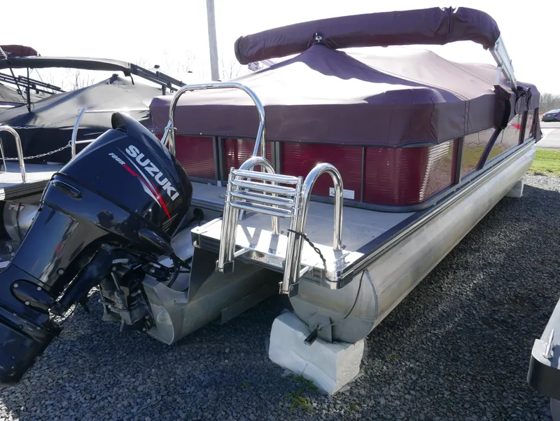 Slide: The Image of 2015 Manitou Oasis pontoon boat with Suzuki outboard motor, parked on gravel. - 4