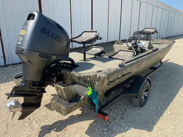 Slide: The Image of 2025 SeaArk Shadow 18 boat with Suzuki engine, parked on gravel near a white building. - 6