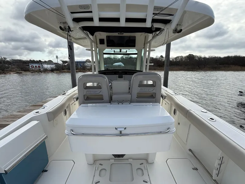 Slide: The Image of 2018 Boston Whaler 330 Outrage boat interior, featuring seating and helm, docked by a calm lake. - 7