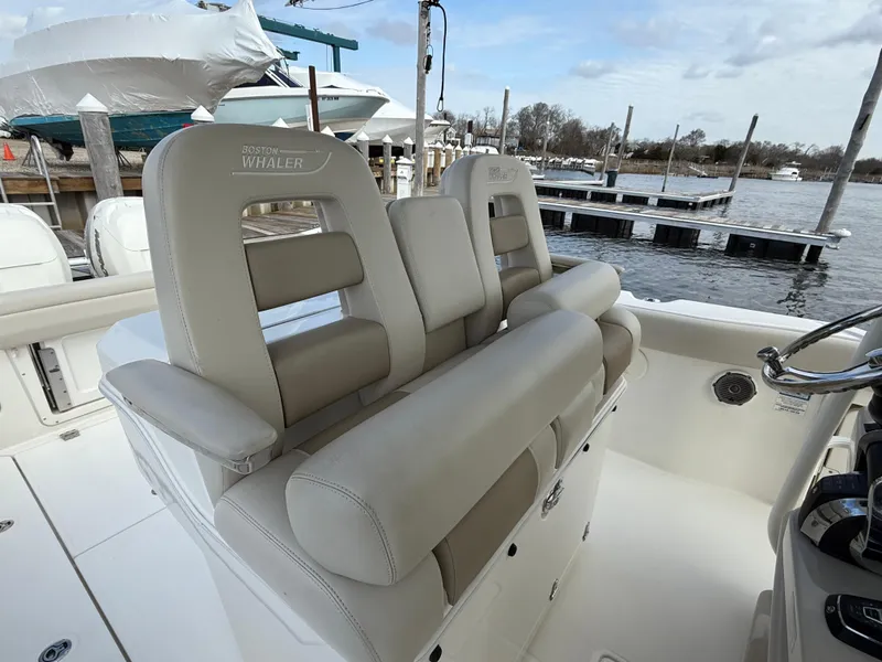Slide: The Image of 2018 Boston Whaler 330 Outrage boat interior with beige seating at a marina. - 9