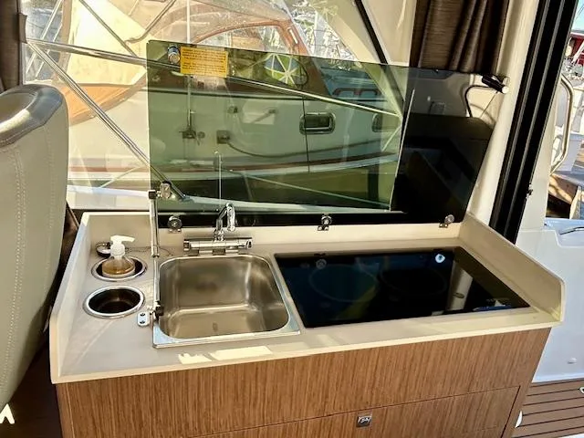 Slide: The Image of 2024 Beneteau Antares 9 boat kitchen with sink, stove, and wooden cabinetry. - 12
