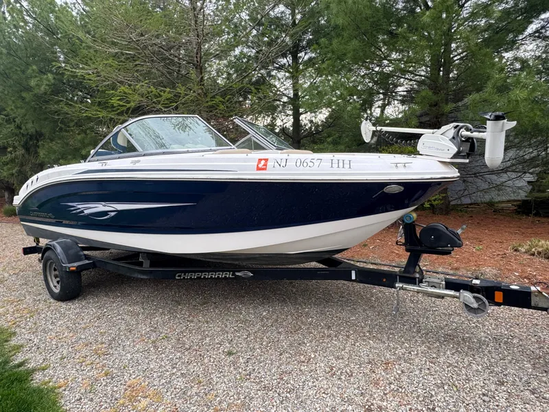 Slide: The Image of 2013 Chaparral 19 Sport H2O boat on trailer, parked on gravel, surrounded by trees. - 0