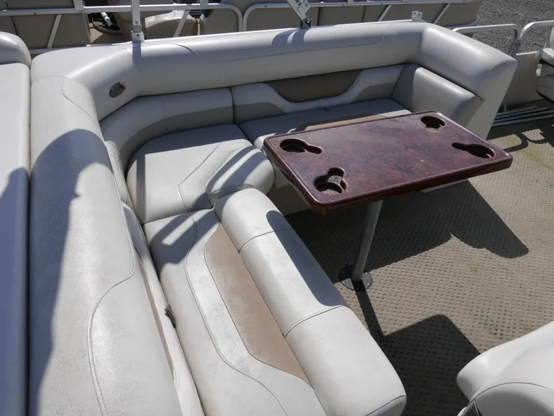 Slide: The Image of 2004 Sylvan Mirage 8522 boat interior with cushioned seating and a wooden table. - 11