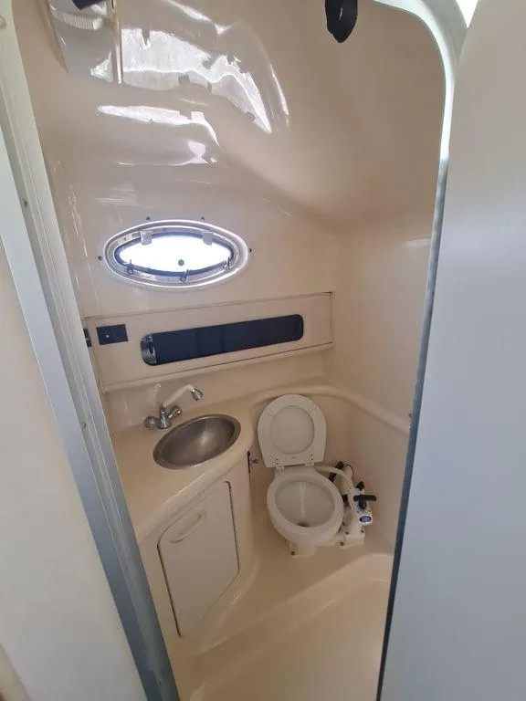 Slide: The Image of 1994 Sea Ray 270 Express boat bathroom with sink, toilet, and porthole window. - 7