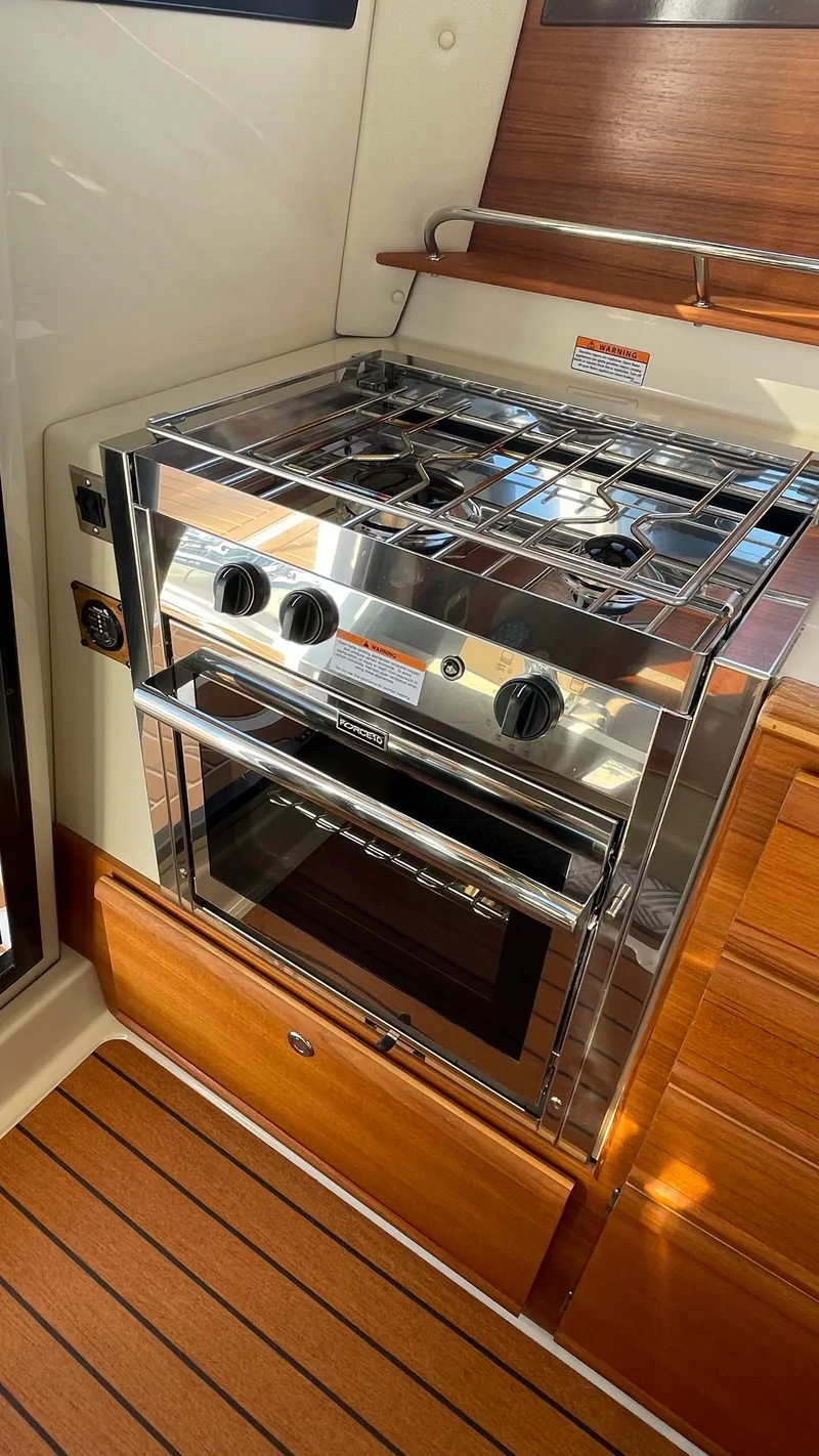 Slide: The Image of 2023 Ranger Tugs R-27 boat kitchen with stainless steel stove and oven, wooden cabinetry. - 17