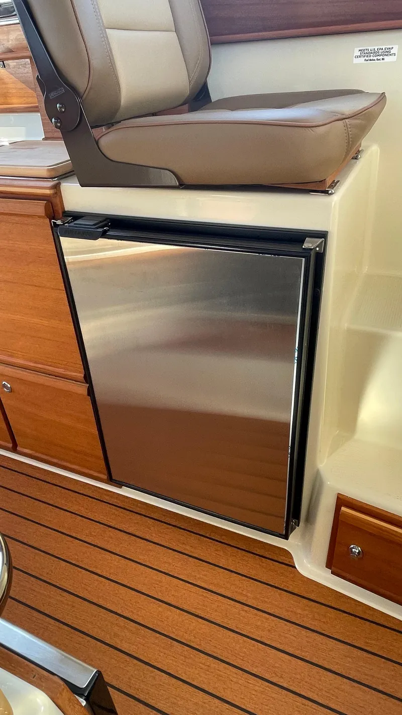 Slide: The Image of 2023 Ranger Tugs R-27 interior with stainless steel mini fridge and wooden flooring. - 26