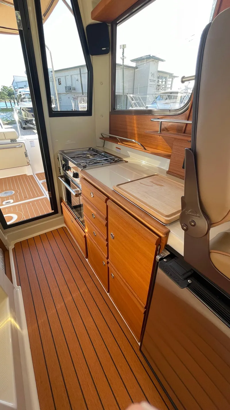 Slide: The Image of 2023 Ranger Tugs R-27 interior with wooden cabinetry and compact kitchen area. - 29