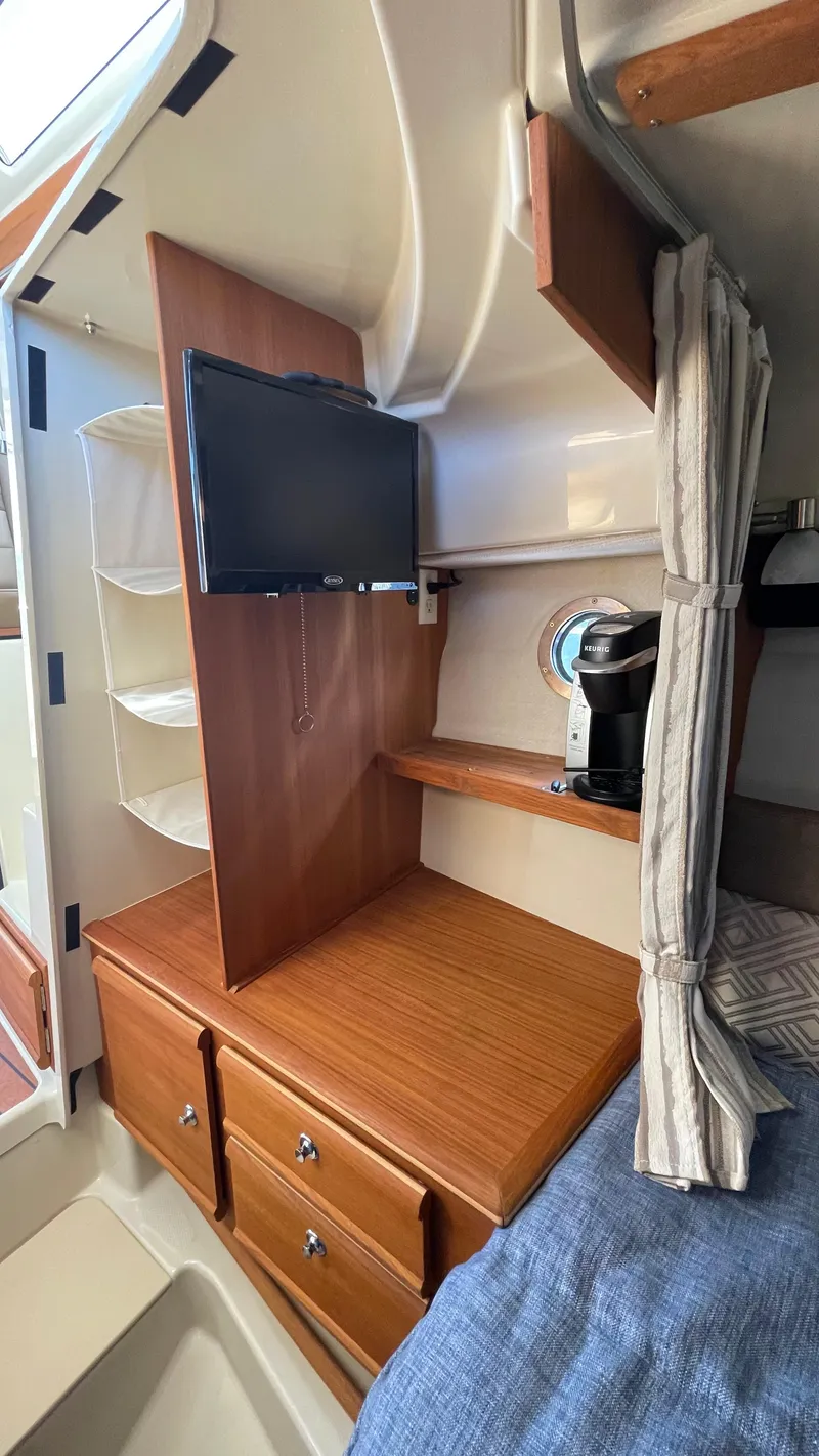 Slide: The Image of 2023 Ranger Tugs R-27 cabin interior with TV, drawers, and cozy bedding. - 34
