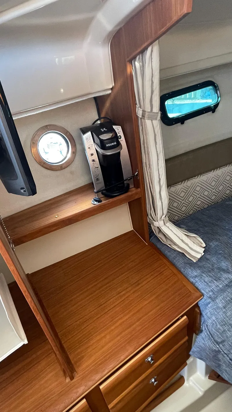 Slide: The Image of 2023 Ranger Tugs R-27 cabin interior with wood finish, coffee maker, and porthole window. - 36