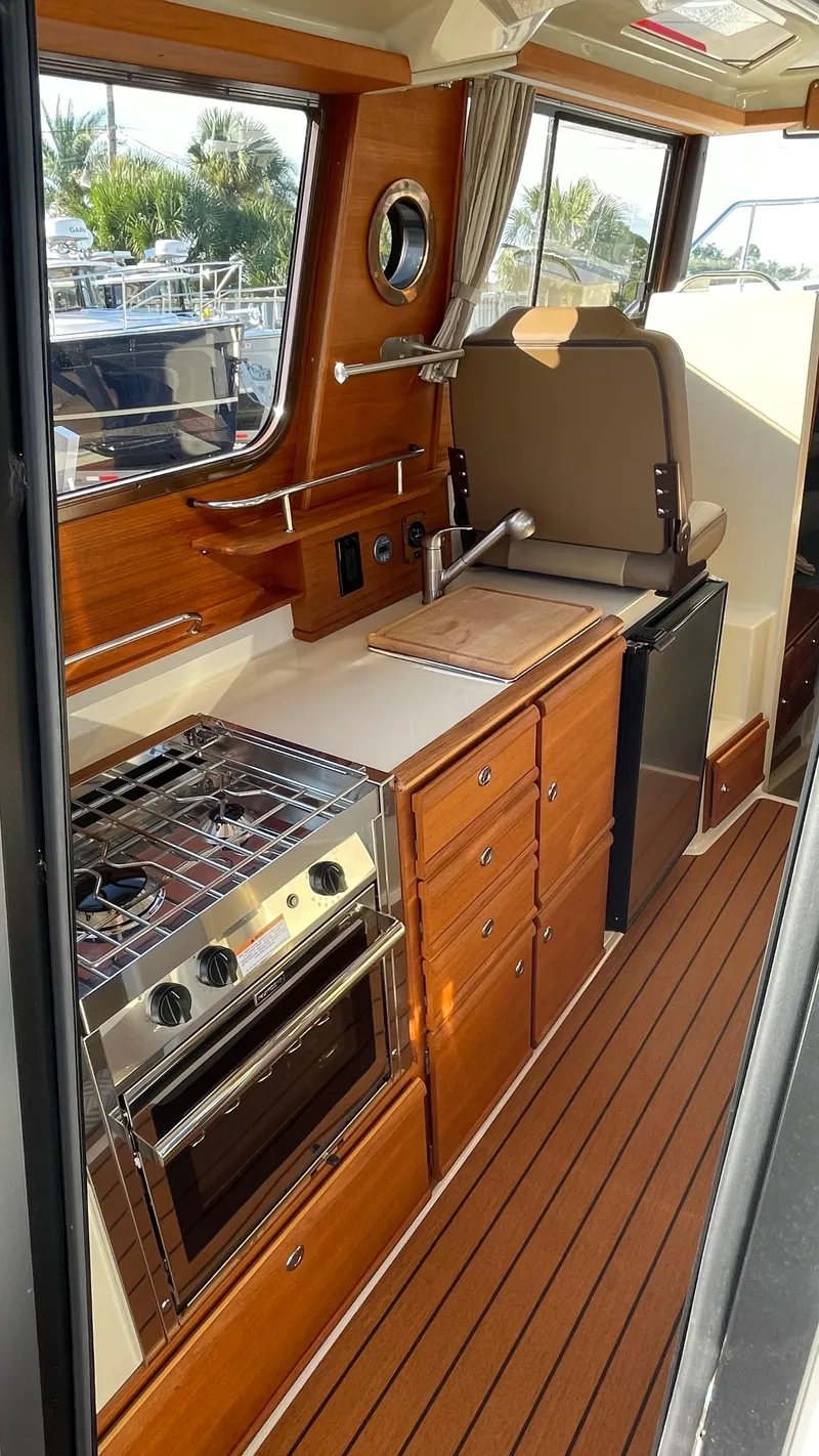 Slide: The Image of 2023 Ranger Tugs R-27 interior kitchen with wood cabinetry and modern appliances. - 49