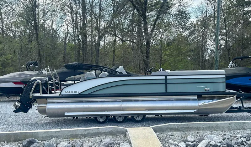 Slide: The Image of 2025 Harris CRUISER 230 SLDH pontoon boat parked on gravel, surrounded by trees. - 6