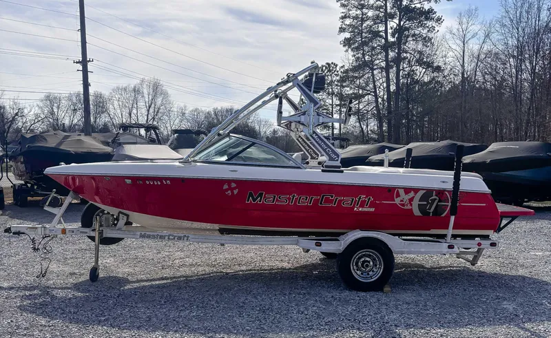 Slide: The Image of 2008 MasterCraft X1 boat in red, parked on a trailer in a gravel lot. - 1