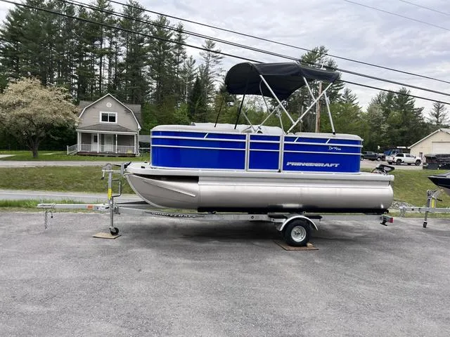 Slide: The Image of 2023 Princecraft Brio E 170 pontoon boat on trailer, parked near houses and trees. - 1