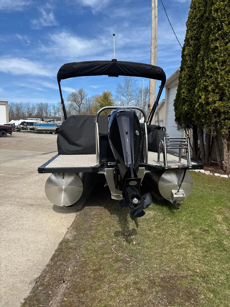 Slide: The Image of 2025 Tahoe Pontoon LTZ Cruise Rear Bench, rear view with motor, parked outdoors. - 5
