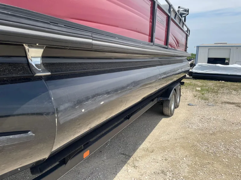 Slide: The Image of 2023 Regency 250 DL3 pontoon boat on trailer, red and black exterior, parked outdoors. - 10