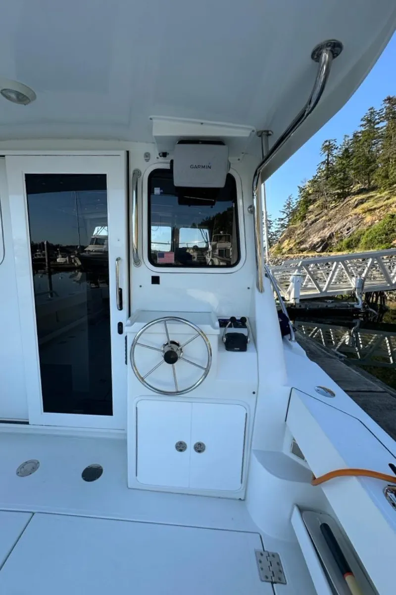 Slide: The Image of 2010 Ocean Sport Roamer boat helm with steering wheel, docked near a scenic shoreline. - 45