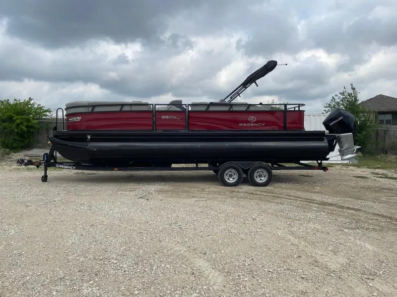 The Image of 2022 Regency 250 DL3 pontoon boat on trailer, parked outdoors under cloudy sky. - 0
