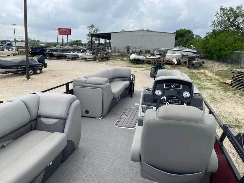 Slide: The Image of 2022 Regency 250 DL3 pontoon boat with spacious seating and modern dashboard in a boatyard. - 18