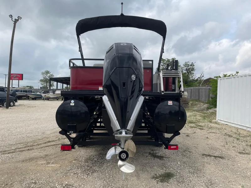 Slide: The Image of 2022 Regency 250 DL3 pontoon boat with outboard motor, parked on gravel lot. - 3
