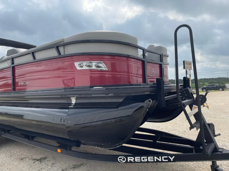 Slide: The Image of 2022 Regency 250 DL3 pontoon boat on trailer, red and black design, cloudy sky background. - 7