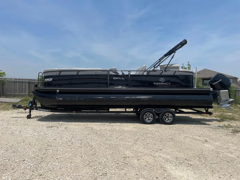 The Image of 2023 Regency 250 LE3 pontoon boat on trailer, parked outdoors. - 0