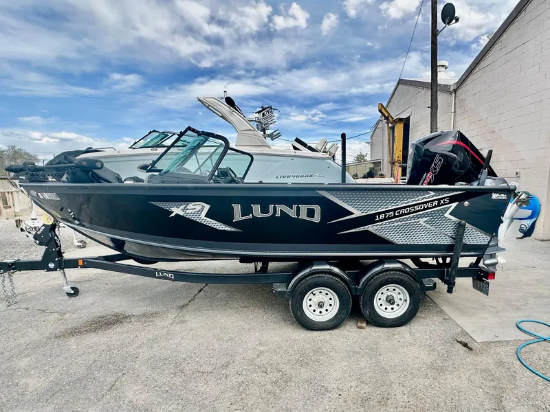 Slide: The Image of 2021 Lund 1875 Crossover XS boat on trailer, parked outdoors under cloudy sky. - 2