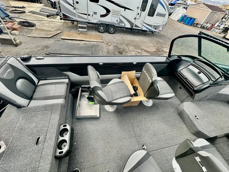 Slide: The Image of 2021 Lund 1875 Crossover XS boat interior with seating and storage, parked near a camper. - 9