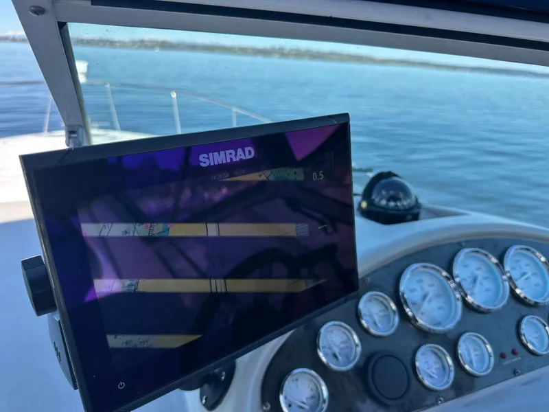 Slide: The Image of 2004 Cruisers Express boat dashboard with Simrad navigation display on calm water. - 15