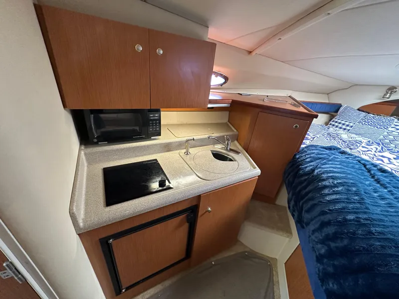 Slide: The Image of 2004 Cruisers Express cabin interior with kitchenette and bed, featuring wood cabinets and modern amenities. - 23
