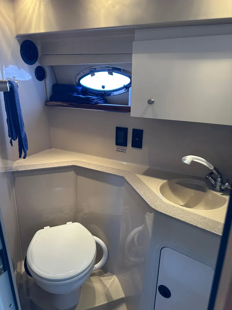 Slide: The Image of 2004 Cruisers Express yacht bathroom with toilet, sink, and porthole window. - 29