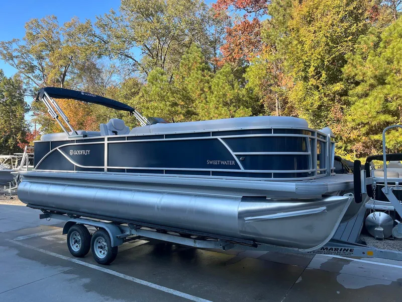 The Image of 2024 Godfrey SWEETWATER 2286 SB pontoon boat on trailer, surrounded by autumn trees. - 0