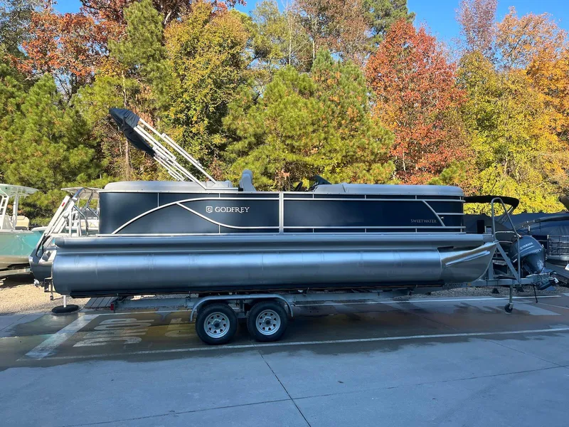 Slide: The Image of 2024 Godfrey SWEETWATER 2286 SB pontoon boat on trailer, surrounded by autumn trees. - 2