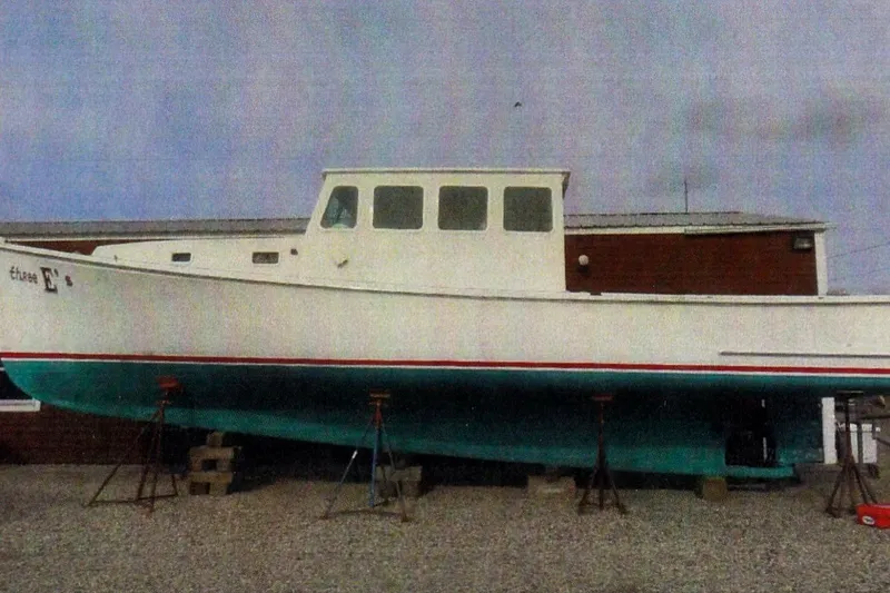 The Image of 1990 BEALS Lobster Boat on stands, white hull, green bottom, gravel ground. - 0
