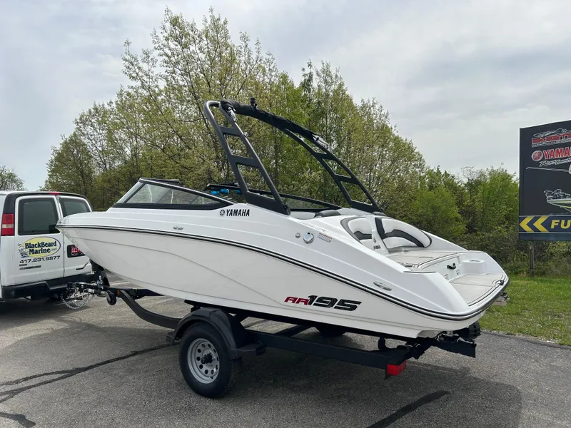 Slide: The Image of 2025 Yamaha Boats AR195 on trailer, sleek white design, parked outdoors. - 2
