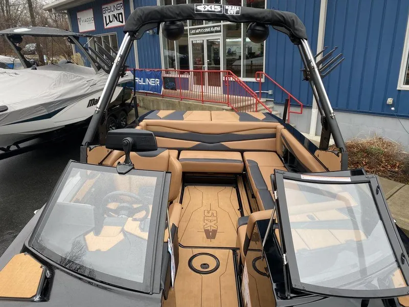 Slide: The Image of 2025 Axis A225 boat interior with tan seating and dual windshields, parked outside a dealership. - 13