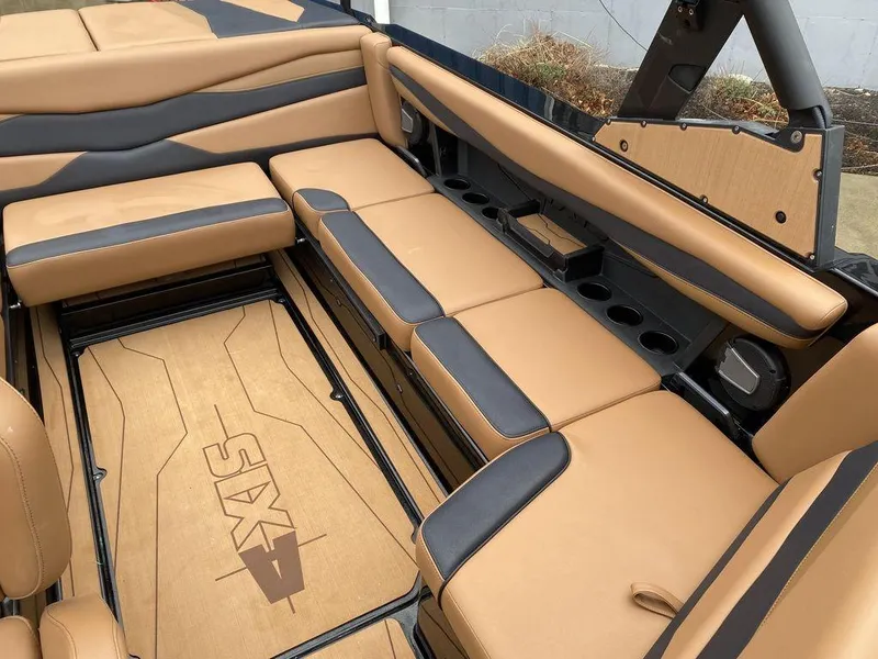 Slide: The Image of 2025 Axis A225 boat interior with tan and gray seating, cup holders, and branded flooring. - 14
