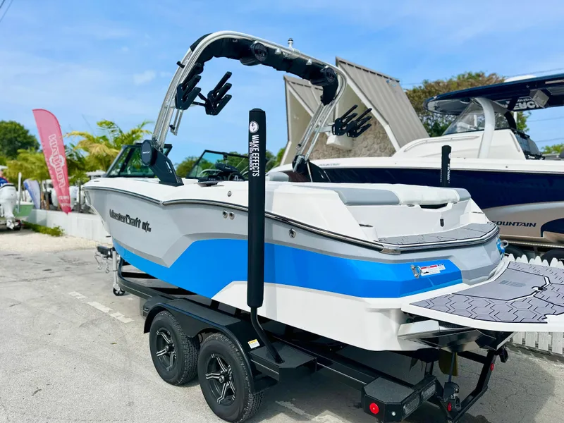 Slide: The Image of 2023 MasterCraft NXT21 boat with blue accents on a trailer, parked outdoors. - 2
