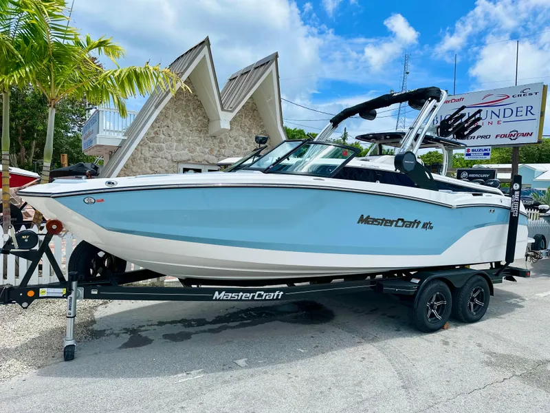 Slide: The Image of 2023 MasterCraft NXT23 boat on trailer, parked outdoors under a clear blue sky. - 1