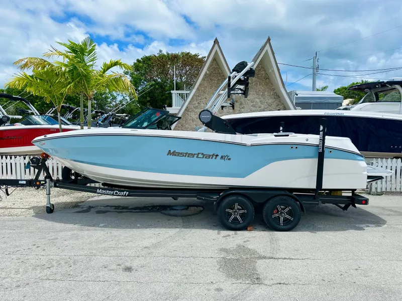Slide: The Image of 2023 MasterCraft NXT23 boat on trailer, parked outdoors under a cloudy sky. - 2