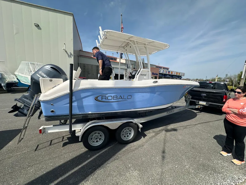 Slide: The Image of 2023 Robalo R202EX boat on trailer, parked outdoors with people nearby. - 3