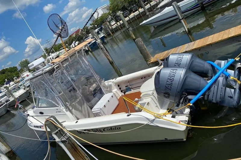 Slide: The Image of 2004 Cobia 270 Walk-Around boat docked with Yamaha engines, clear skies, and marina background. - 0