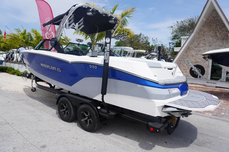 Slide: The Image of 2023 MasterCraft NXT24 boat on trailer, blue and white design, parked outdoors. - 38