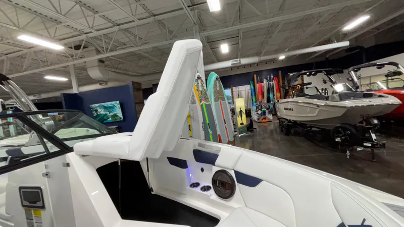 Slide: The Image of 2025 MasterCraft XT23 boat interior in showroom with surfboards and other boats. - 23