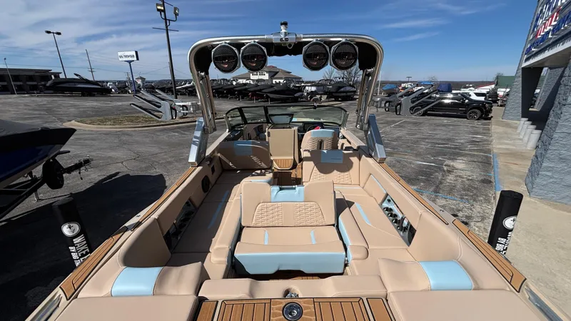 Slide: The Image of 2025 MasterCraft X26 boat interior with beige and blue seating, parked outdoors. - 15