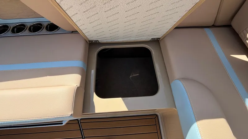 Slide: The Image of 2025 MasterCraft X26 boat interior storage compartment with beige and blue seating. - 18
