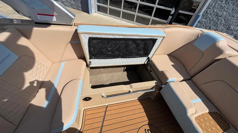 Slide: The Image of 2025 MasterCraft X26 boat interior with beige seating and open storage compartment. - 20