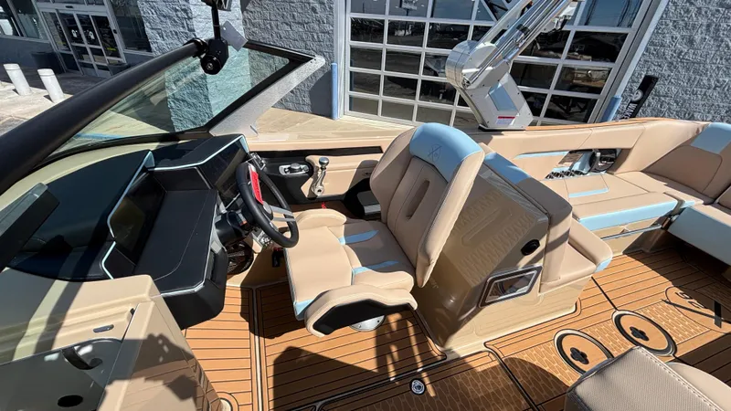 Slide: The Image of 2025 MasterCraft X26 boat interior with tan and blue seating, modern dashboard, and wood flooring. - 24