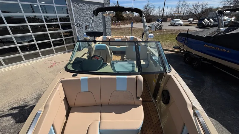 Slide: The Image of 2025 MasterCraft X26 boat with beige seating and glass windshield, parked outdoors. - 39