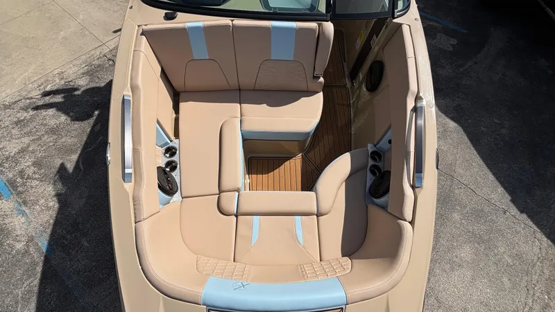 Slide: The Image of 2025 MasterCraft X26 boat interior with beige and blue seating, featuring cup holders and wood flooring. - 40