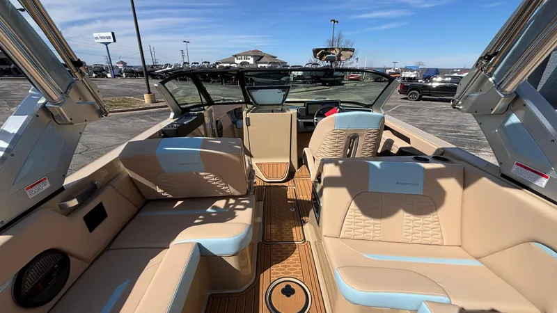 Slide: The Image of 2025 MasterCraft X26 boat interior with beige and blue seating, parked outdoors. - 8